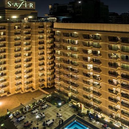 Safir Hotel Cairo Giza Exterior photo The photo shows a multi-story hotel building at night. The building is illuminated, showcasing multiple balconies along its facade. In front of the hotel, there is an outdoor area with seating arranged around a pool, which is also lit up. The hotel's