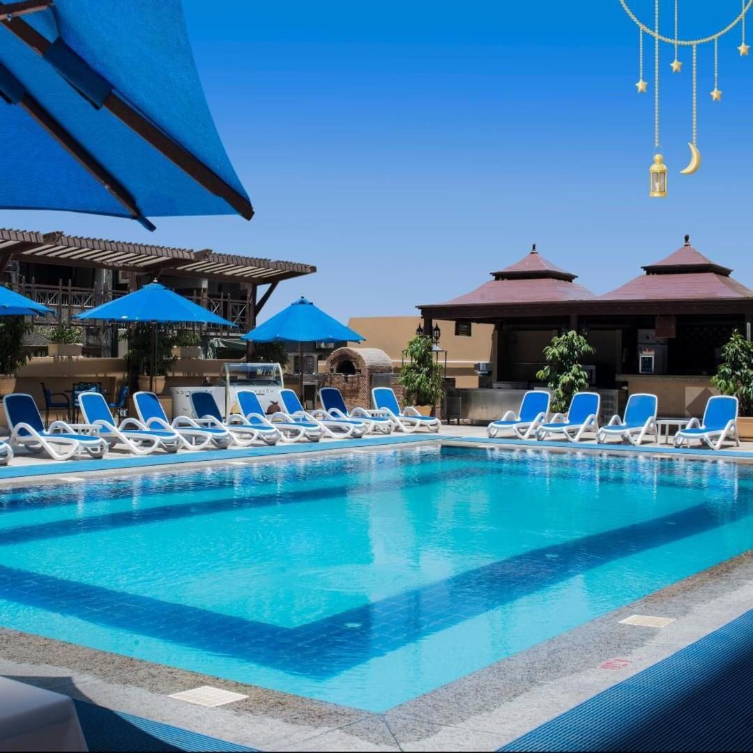 Safir Hotel Cairo Giza Exterior photo The photo showcases a bright, inviting swimming pool surrounded by lounging chairs. The pool is set in a sunny outdoor area, with clear blue water reflecting the sky. There are several blue umbrellas providing shade over the lounge chairs, which are 