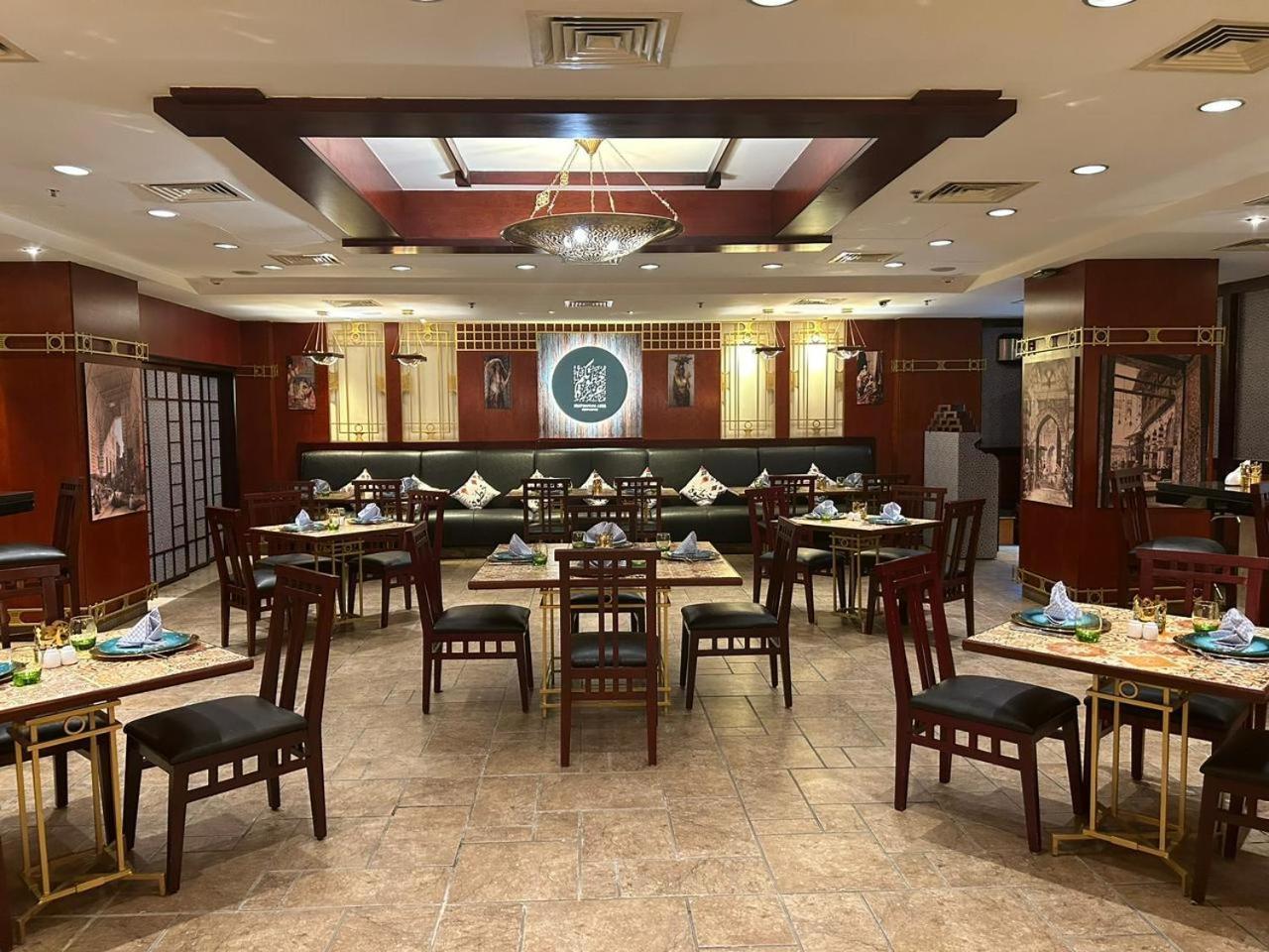 Safir Hotel Cairo Giza Exterior photo The photo shows the interior of a restaurant. The space features a combination of warm wood tones and elegant decorations. There are several dining tables arranged throughout, each set with plates, cutlery, and decorative napkins. The walls are adorn