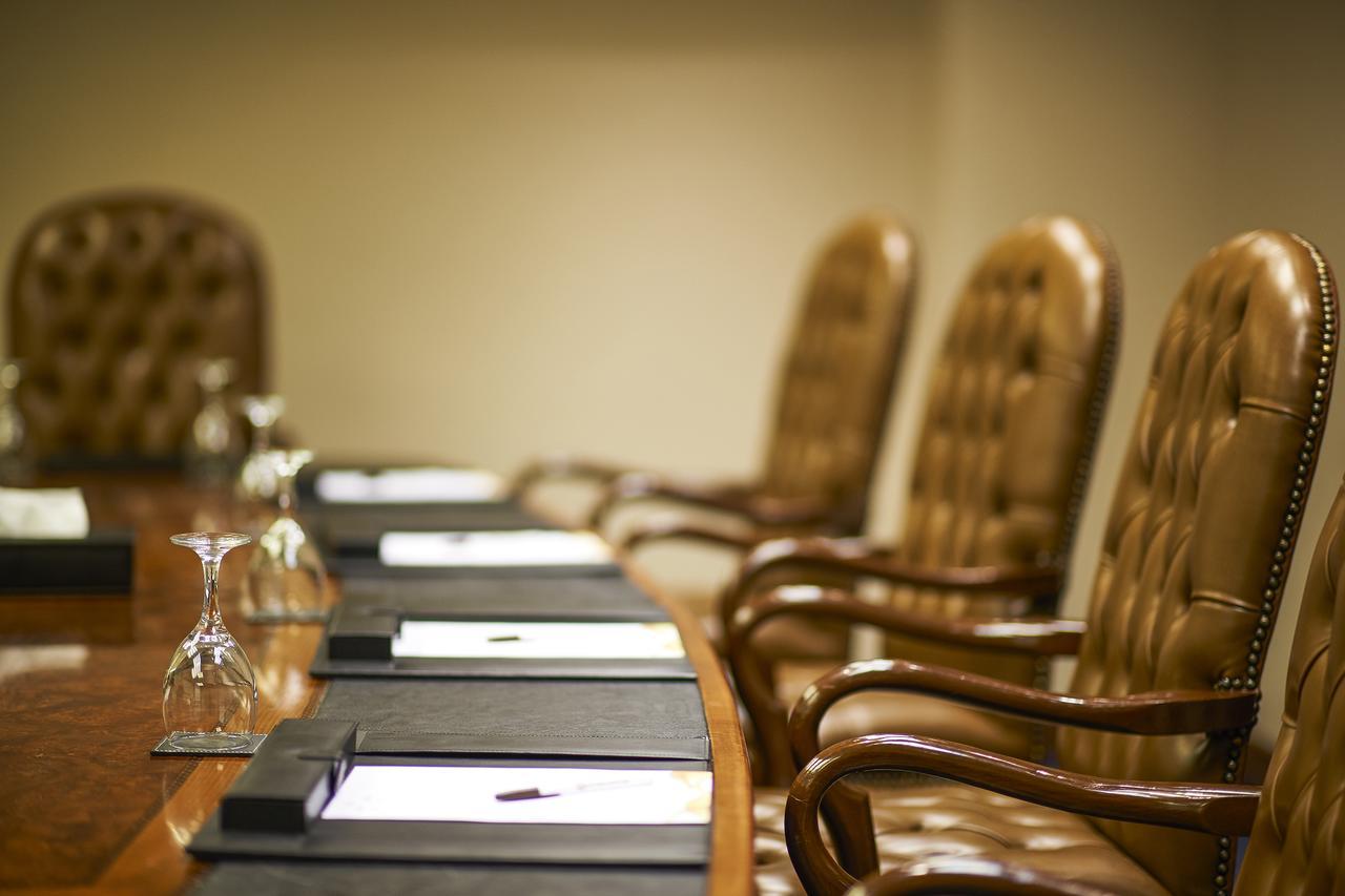 Safir Hotel Cairo Giza Exterior photo The photo shows a conference room setting with a long wooden table and several high-backed chairs. The chairs appear to be upholstered in a brown leather material. Each place at the table has a black folder or pad, and there are also glass water gobl