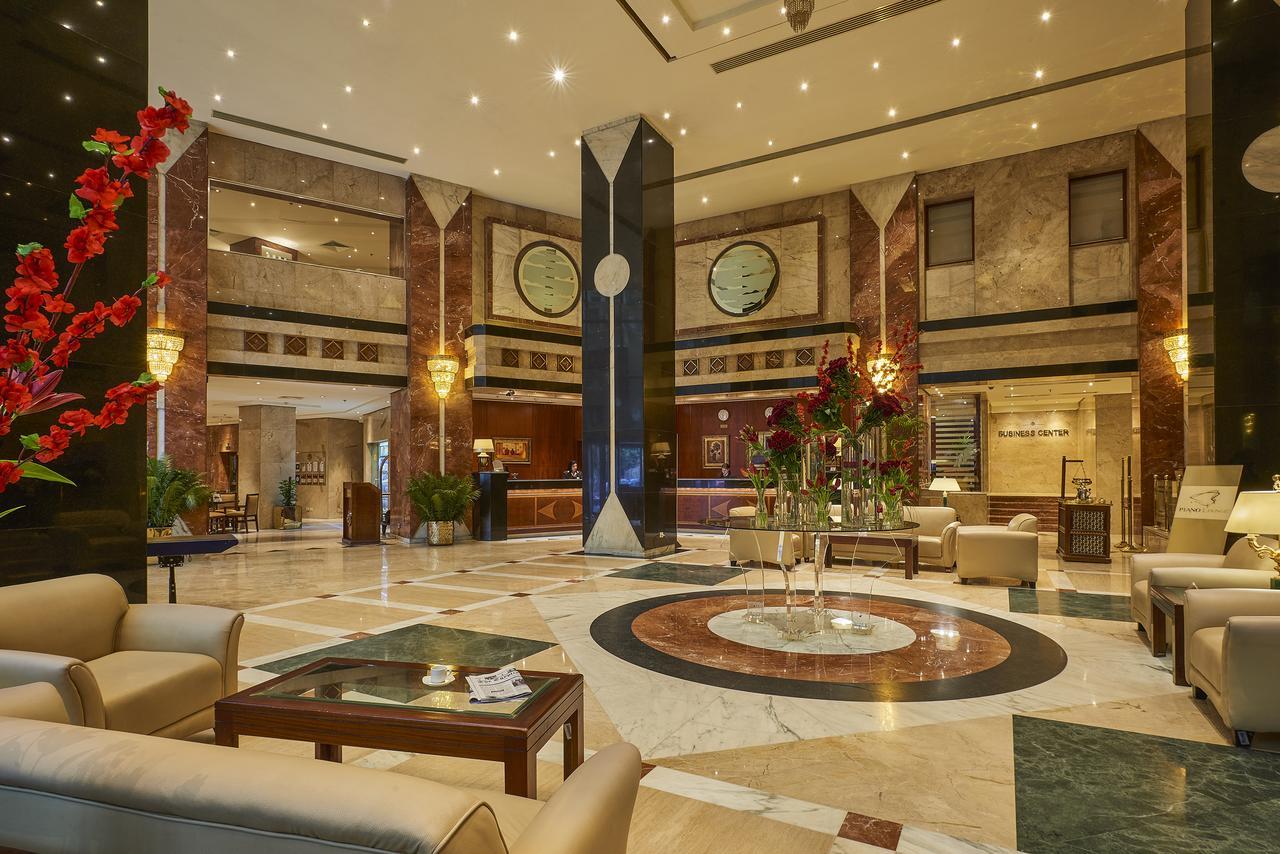 Safir Hotel Cairo Giza Exterior photo The photo shows a luxurious hotel lobby. The space features elegant marble flooring with a circular design at the center. There are comfortable seating arrangements with light-colored sofas and wooden coffee tables. Lush green plants and vibrant flor