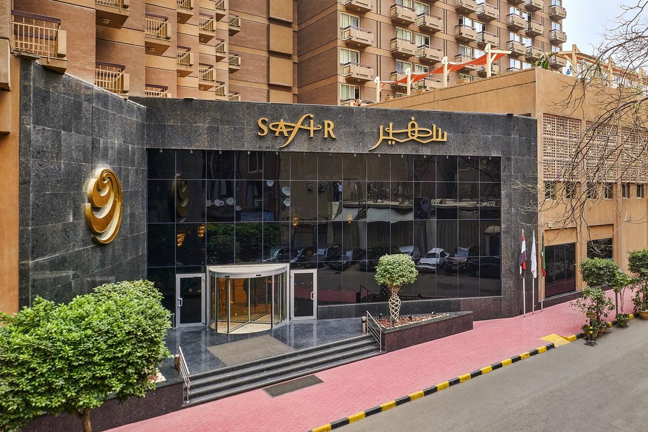 Safir Hotel Cairo Giza Exterior photo The photo depicts the entrance of a modern building, which appears to be a hotel or a commercial establishment. The facade features a large glass front with reflective surfaces. Above the entrance, there is a prominent sign displaying the name of the