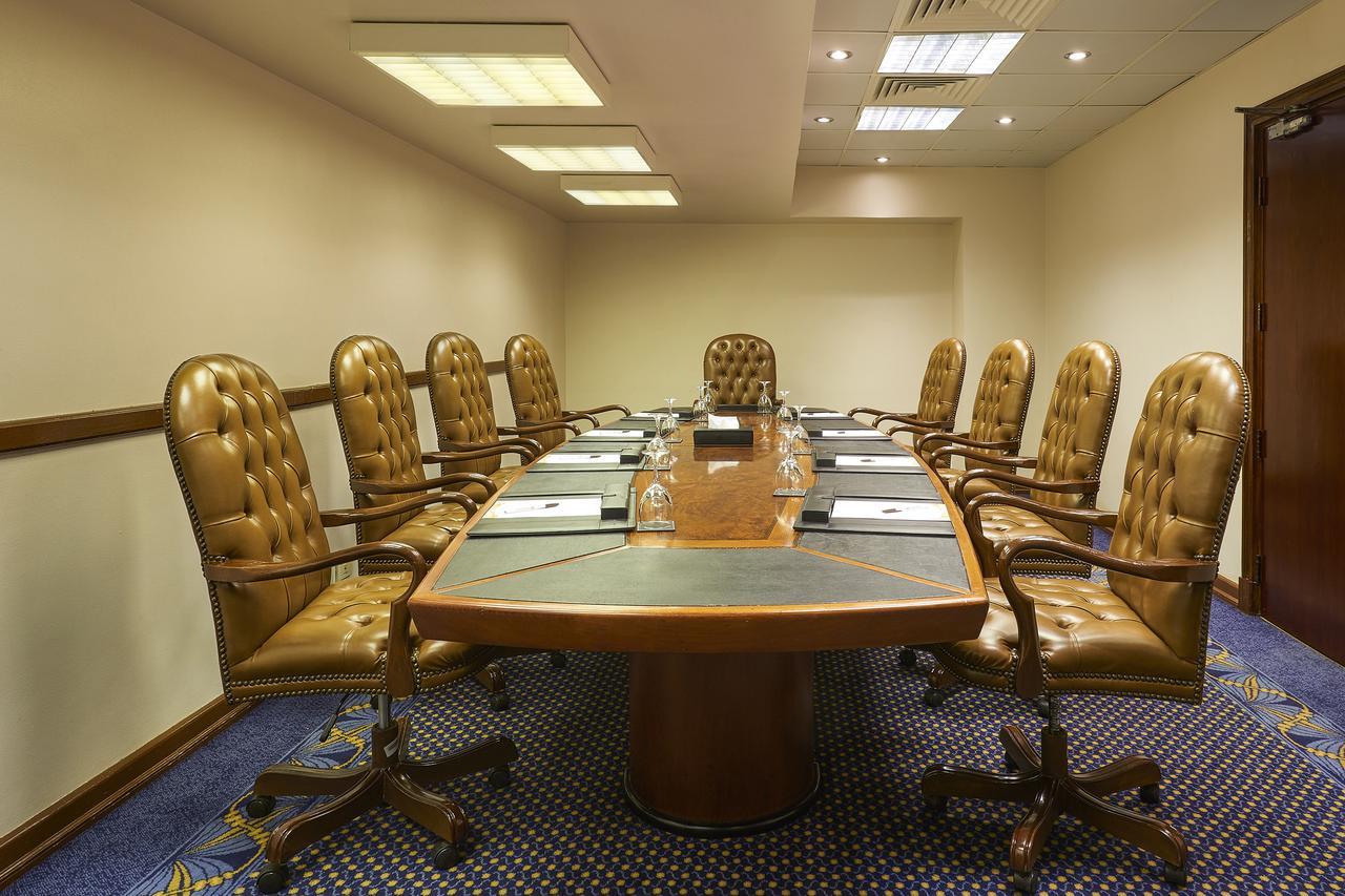 Safir Hotel Cairo Giza Exterior photo The photo shows a conference room with a large oval table surrounded by several brown leather chairs. There are eight chairs in total, each with a high back and wheels. The table has some notepads and glasses of water set up on it. The room has neutr