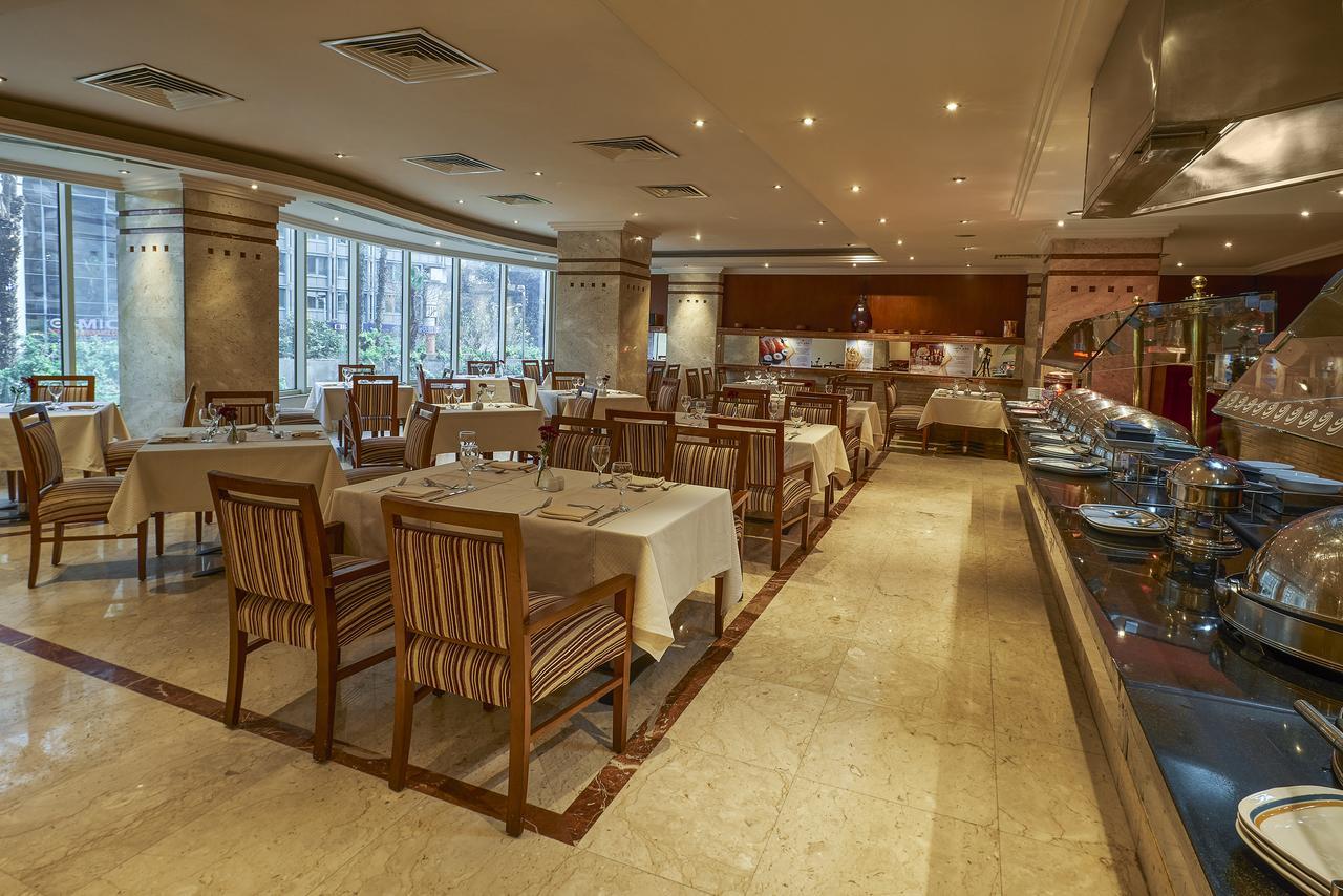 Safir Hotel Cairo Giza Exterior photo The photo shows the interior of a restaurant. It features a spacious dining area with several tables laid out with white tablecloths. The tables are accompanied by wooden chairs that have striped patterns. The restaurant is well-lit with soft lightin