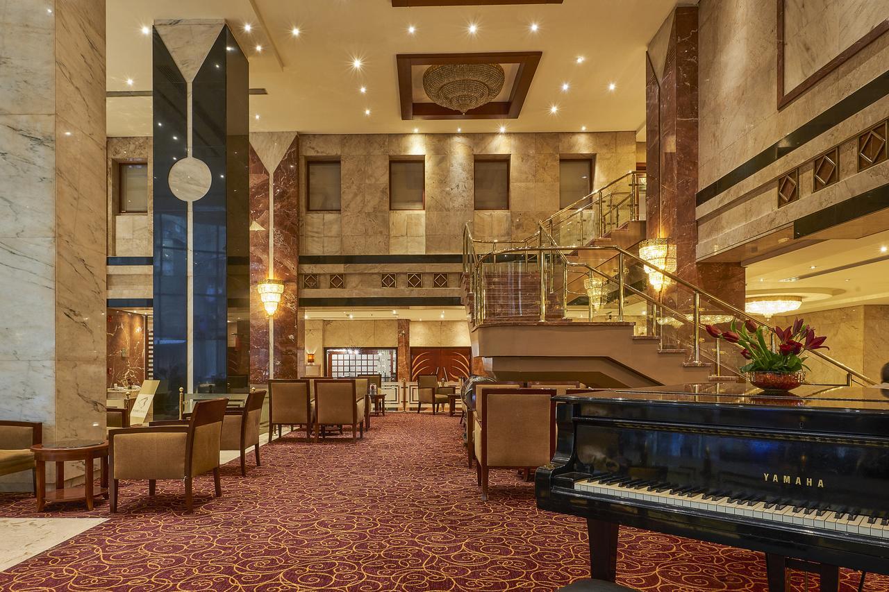 Safir Hotel Cairo Giza Exterior photo The image shows an elegant hotel lobby. The space features marble walls and a plush carpet, giving it a luxurious feel. There are seating areas with comfortable chairs arranged around tables. A grand staircase leads to an upper level, and large windo